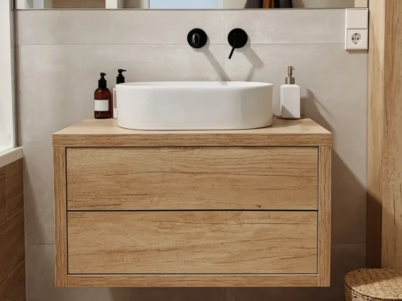 Wood bathroom sink unit with drawers and black tapware.