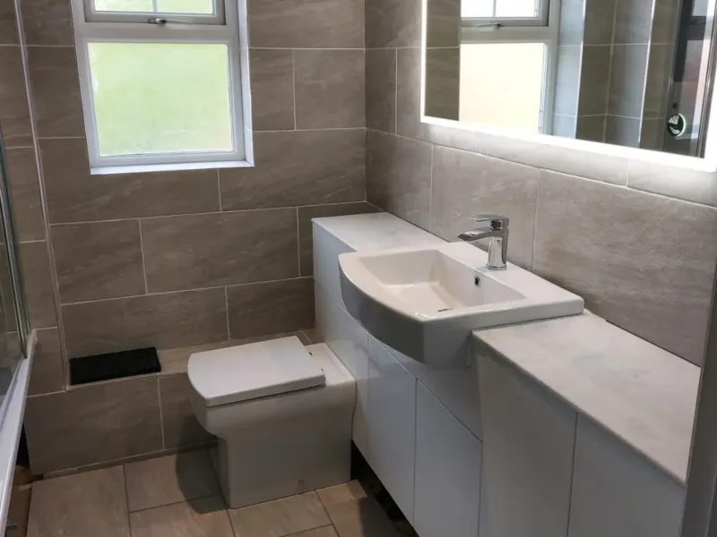 White bathroom unit with a square shaped sink basin and toilet under a LED mirror.