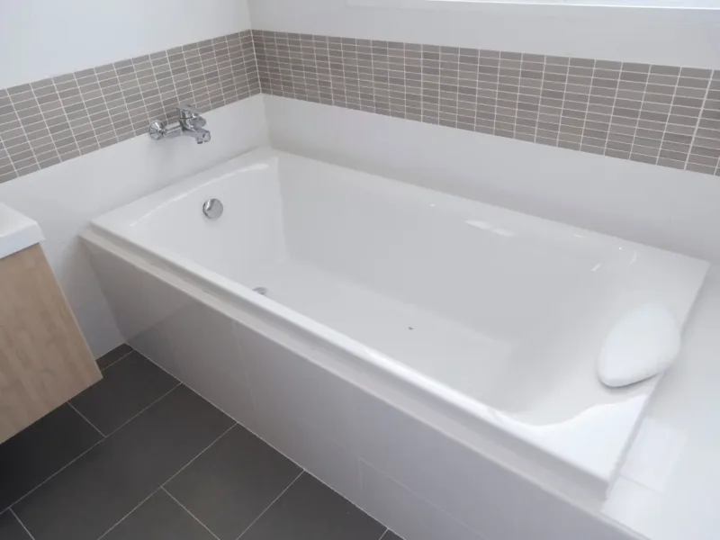 White fitted square shaped bathtub surrounded by white tiled walls.